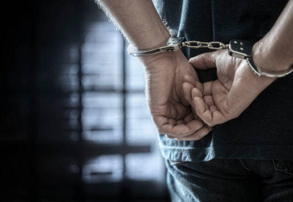 Arrested man in handcuffs with handcuffed hands behind back in prison